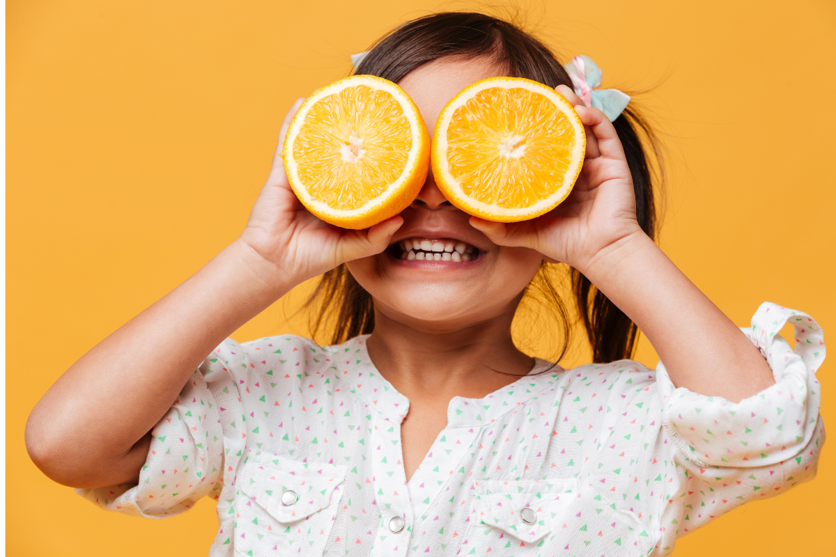 κορίτσι με κοτσιδάκια κρατά κομμένο πορτοκάλι μπροστά από τα μάτια του