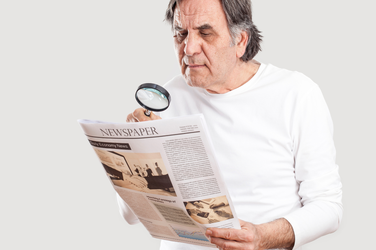 μεσήλικας άντρας κοιτάζει με μεγεθυντικό φακό την εφημερίδα