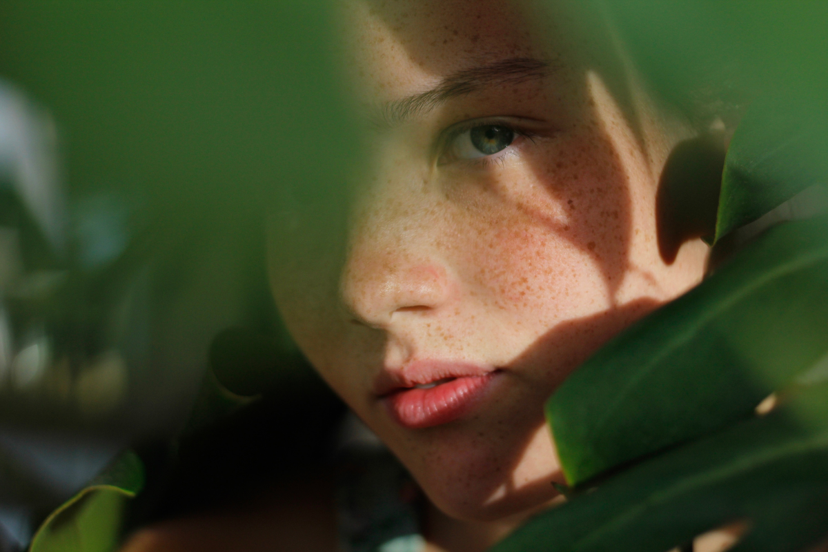 girl with freckles hiding among leaves