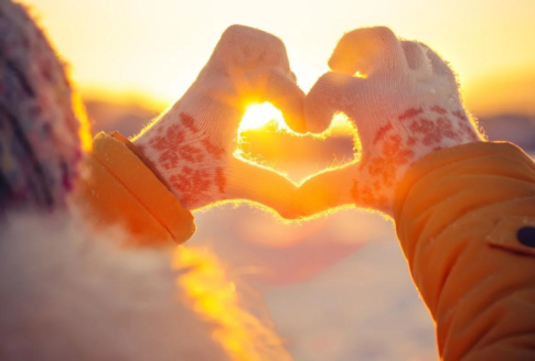 χέρια με γάντια σχηματίζουν καρδιά στον ήλιο σε χειμωνιάτικο τοπίο