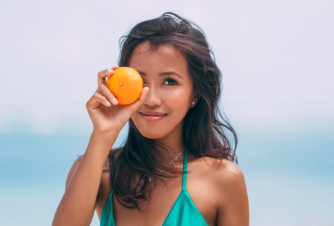 μαυρισμένη γυναίκα με μαγιό στην παραλία κρατά πορτοκάλι