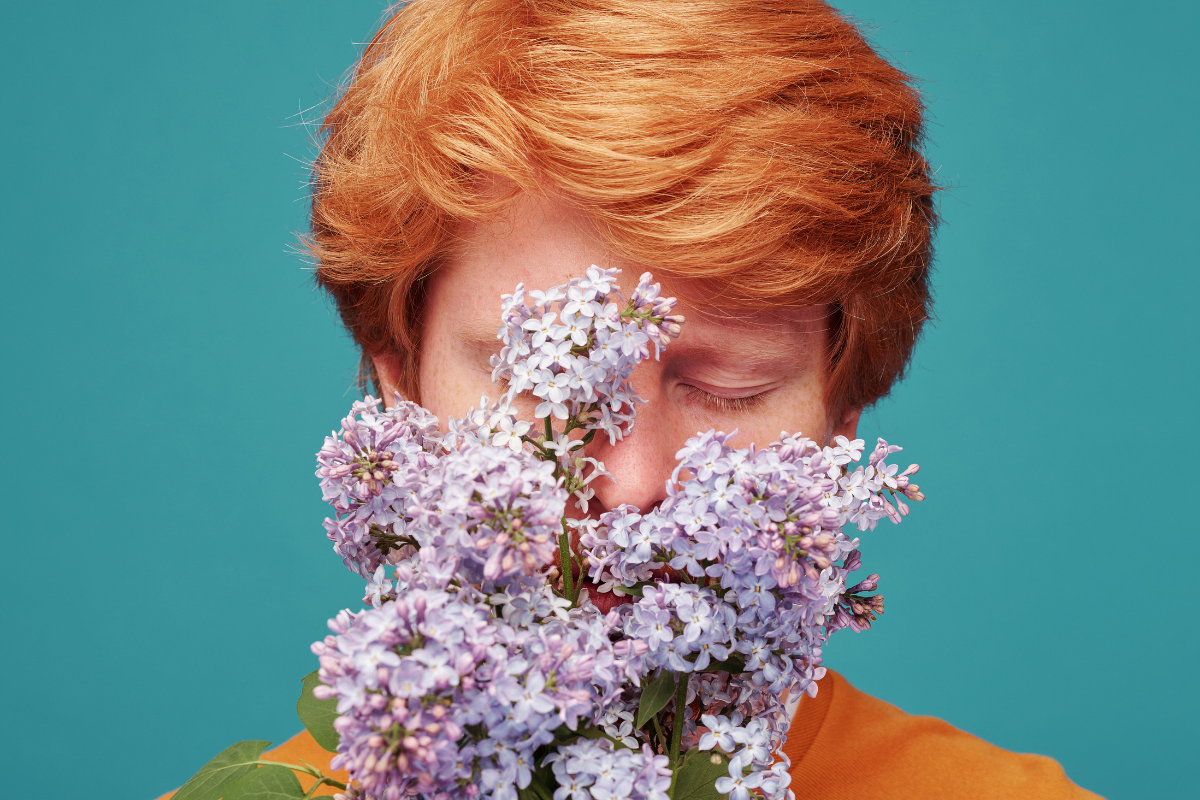 Άντρας με κόκκινα μαλλιά ο οποίος κρατάει λουλούδια κοντά στο πρόσωπό του.