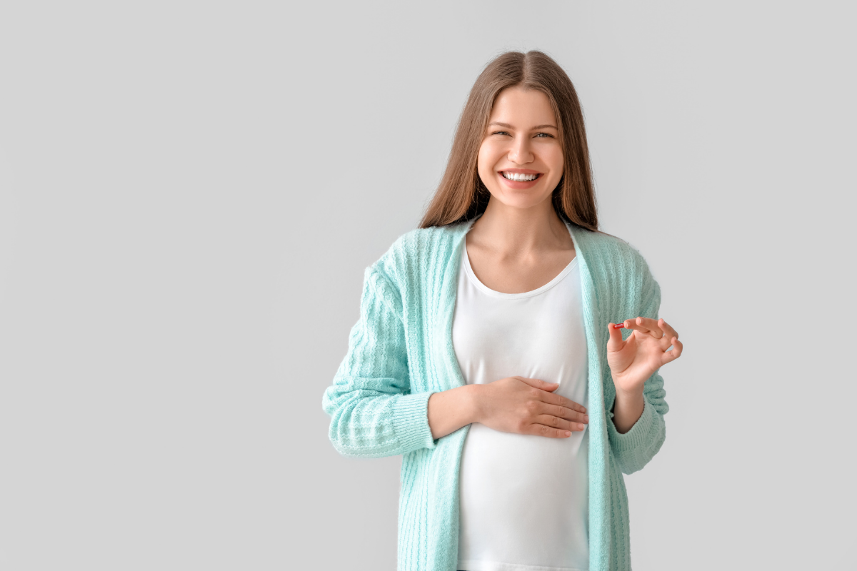 Νεαρή έγκυος με συμπλήρωμα διατροφής στο δεξί χέρι.