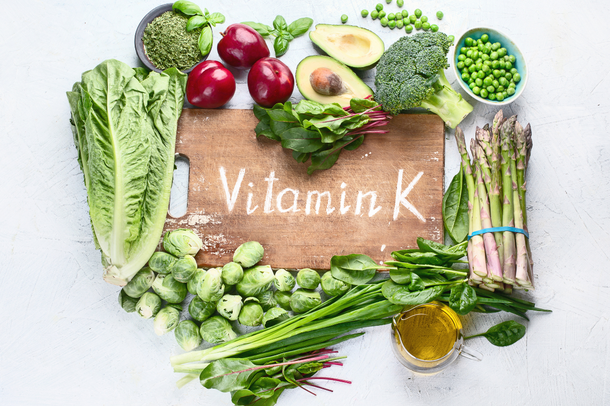 leafy greens and fruits around wood ton which Vitamin K is written