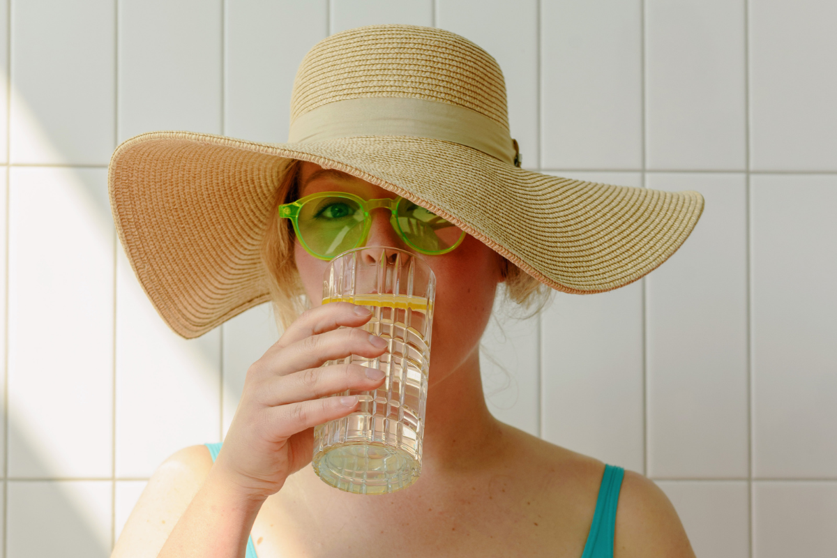 γυναίκα με ψάθινο καπέλο & πράσινα γυαλιά πίνει νερό