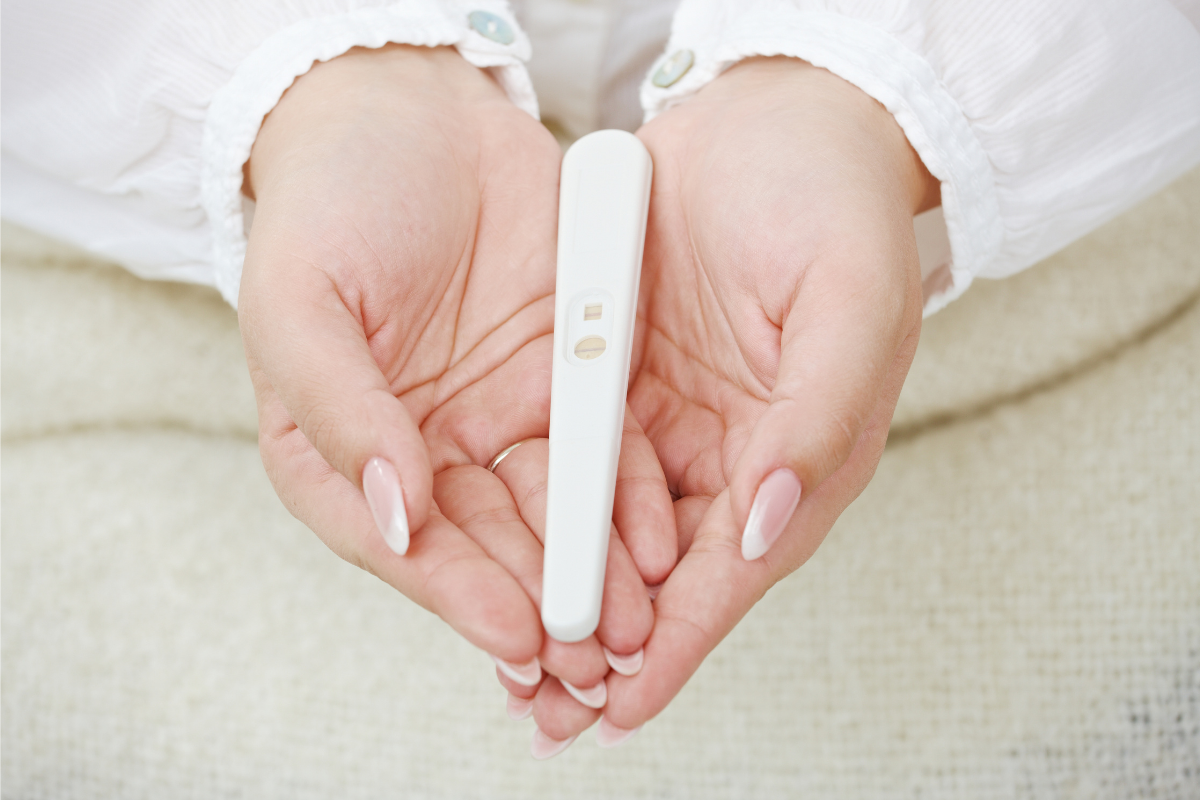χέρια γυναίκας σε σχήμα καρδιάς που κρατάνε τεστ εγκυμοσύνης