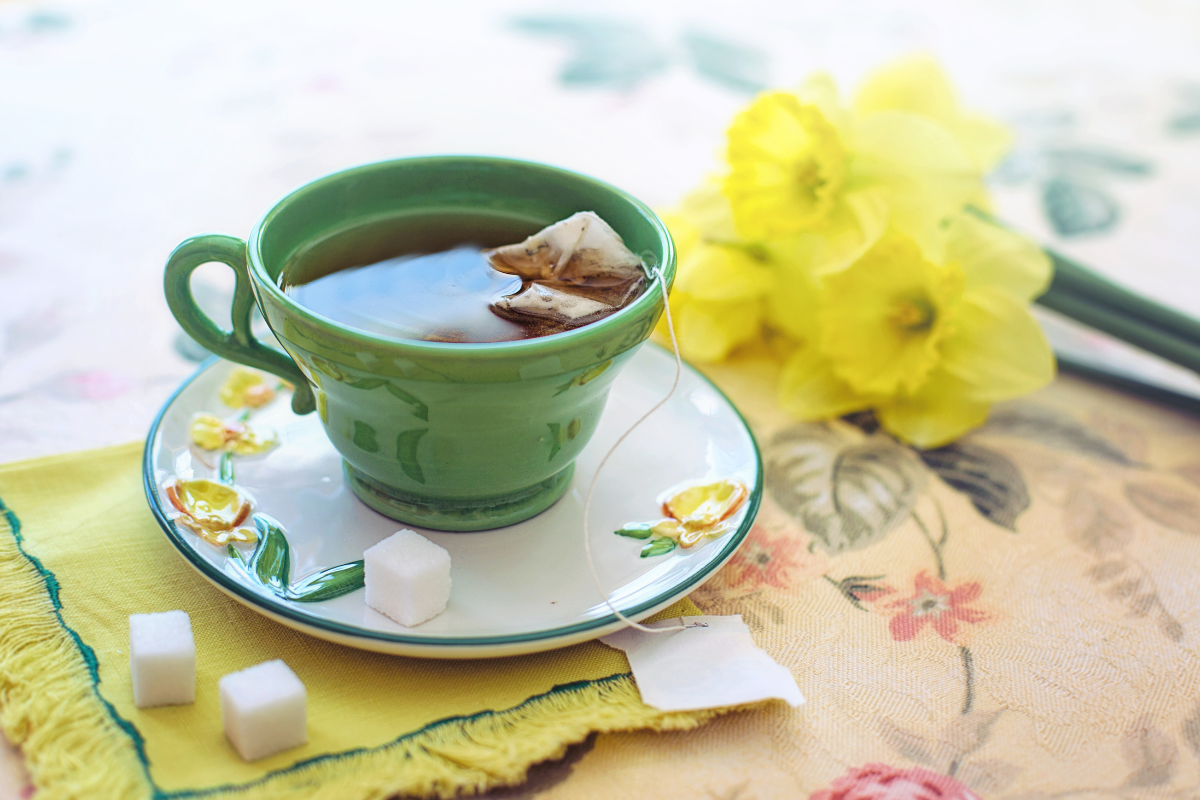 τσάι σε φλιτζάνι δίπλα σε κίτρινο λουλούδι και ζαχαρίνες