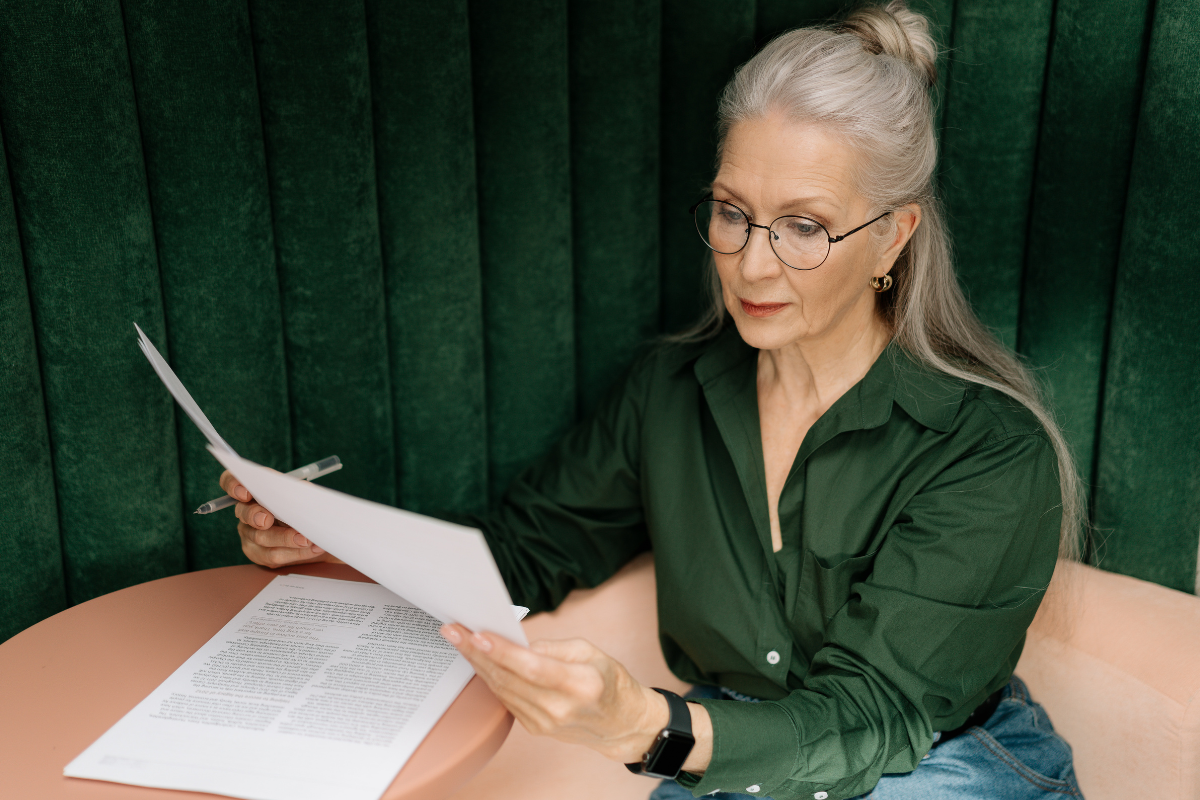 ηλικιωμένη μοντέρνα γυναίκα φοράει γυαλιά και διαβάζει ένα φύλλο