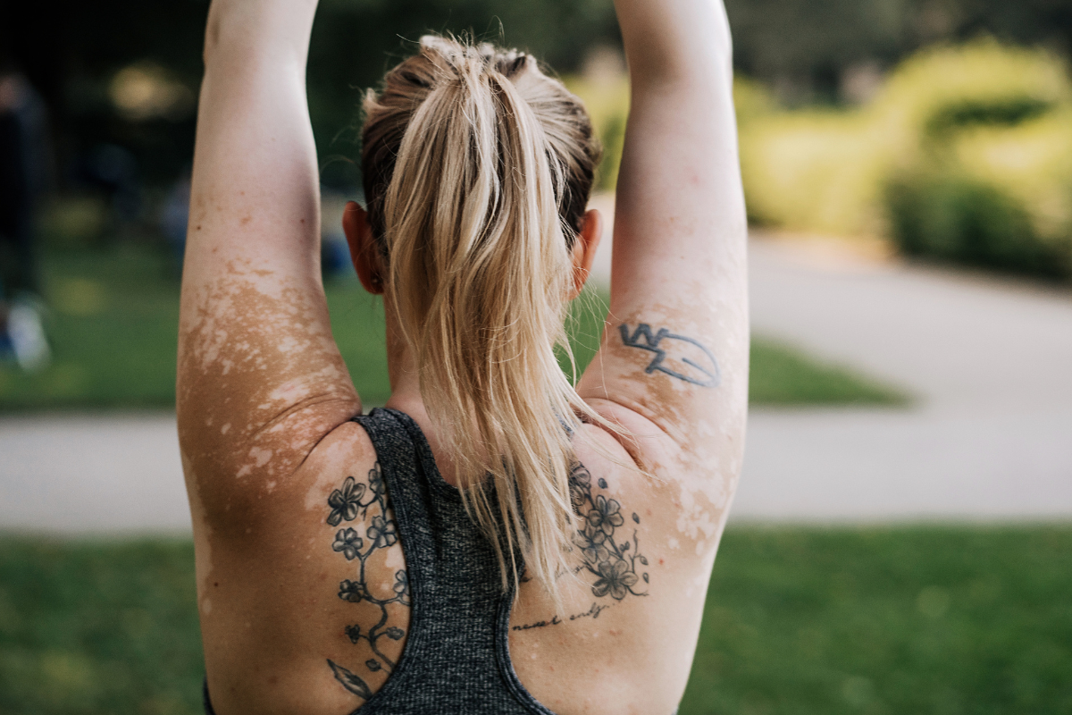 ξανθιά γυναίκα με λεύκη και τατουάζ στην πλάτη κάνει stretching στο πάρκο