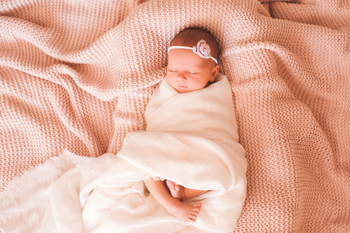 μωρό κοριτσάκι με κορδέλα στα μαλλιά κοιμάται τυλιγμένο σε λευκό ύφασμα