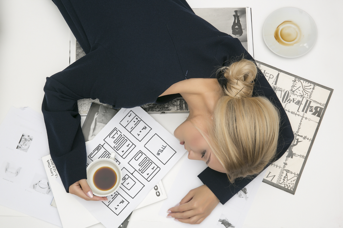 ξανθιά γυναίκα κοιμάται πάνω σε σχέδια με καφέ στο χέρι