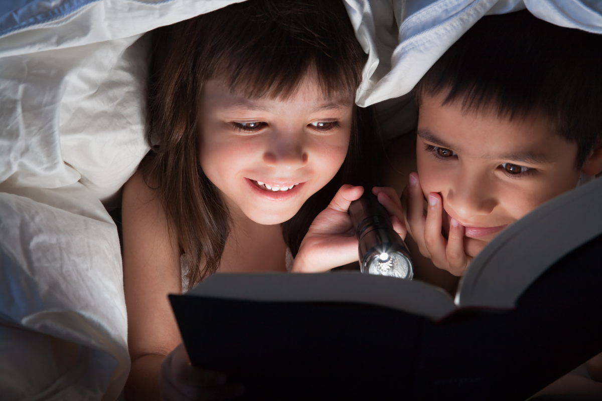 2 παιδιά διαβάζουν με φακό κάτω από το πάπλωμα