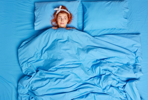 γυναίκα ξαπλώνει σε κρεβάτι σκεπασμένη με τιρκουάζ κλινοσκεπάσματα