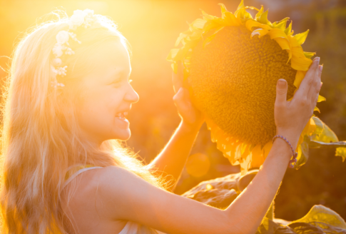 ξανθό κορίτσι με λουλούδια στα μαλλιά κρατά ηλίανθο στον ήλιο