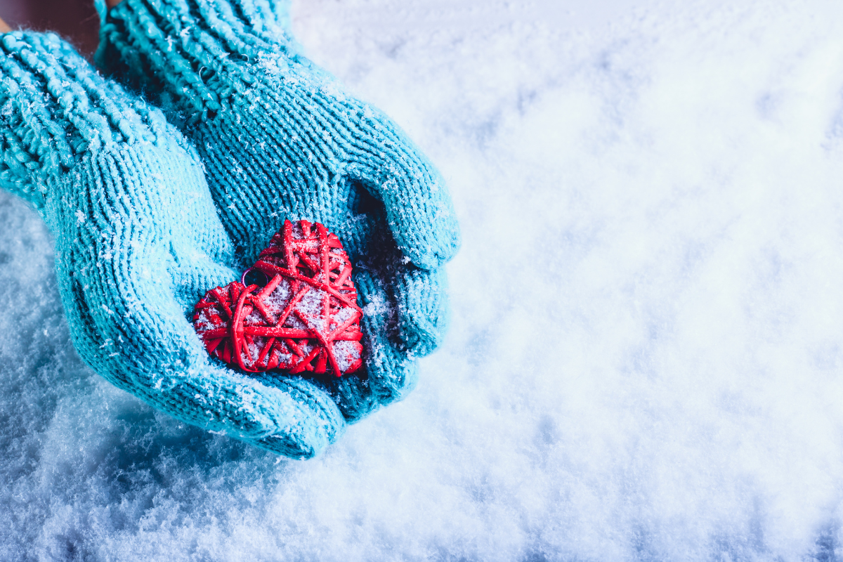 χέρια με γαλάζια γάντια κρατούν κόκκινη καρδιά στα χιόνια