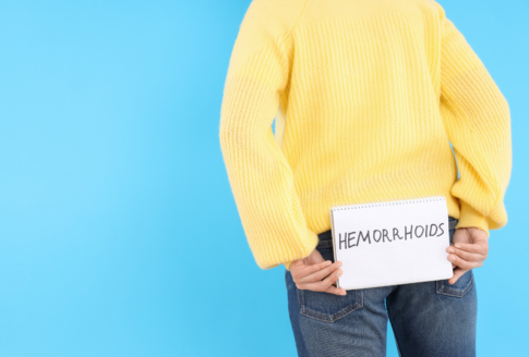 γυναίκα με κίτρινο πουλόβερ κρατά χαρτί που γράφει hemorrhoids πίσω από την πλάτη