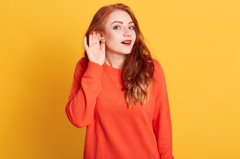 κοκκινομάλα κοπέλα με πορτοκαλί πουλόβερ προσπαθεί να ακούσει