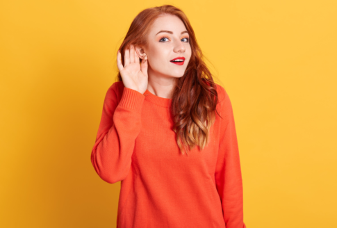 κοκκινομάλα κοπέλα με πορτοκαλί πουλόβερ προσπαθεί να ακούσει