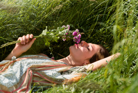 γυναίκα ξαπλώνει στο γρασίδι & μυρίζει ένα λουλούδι