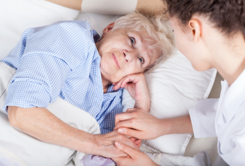 γιαγιά με κατάκλιση στο κρεβάτι κρατάει το χέρι νοσοκόμας