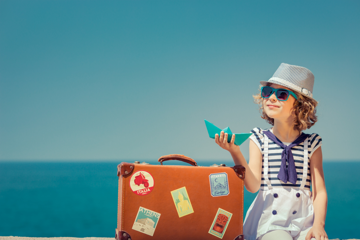 little girl seats next to her suitcase with sea background