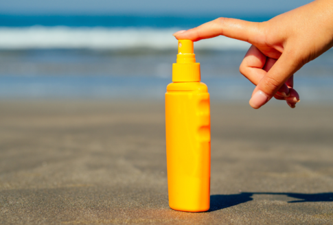 αντηλιακό σε κίτρινο μπουκάλι πάνω στην άμμο με χέρι να το πατάει