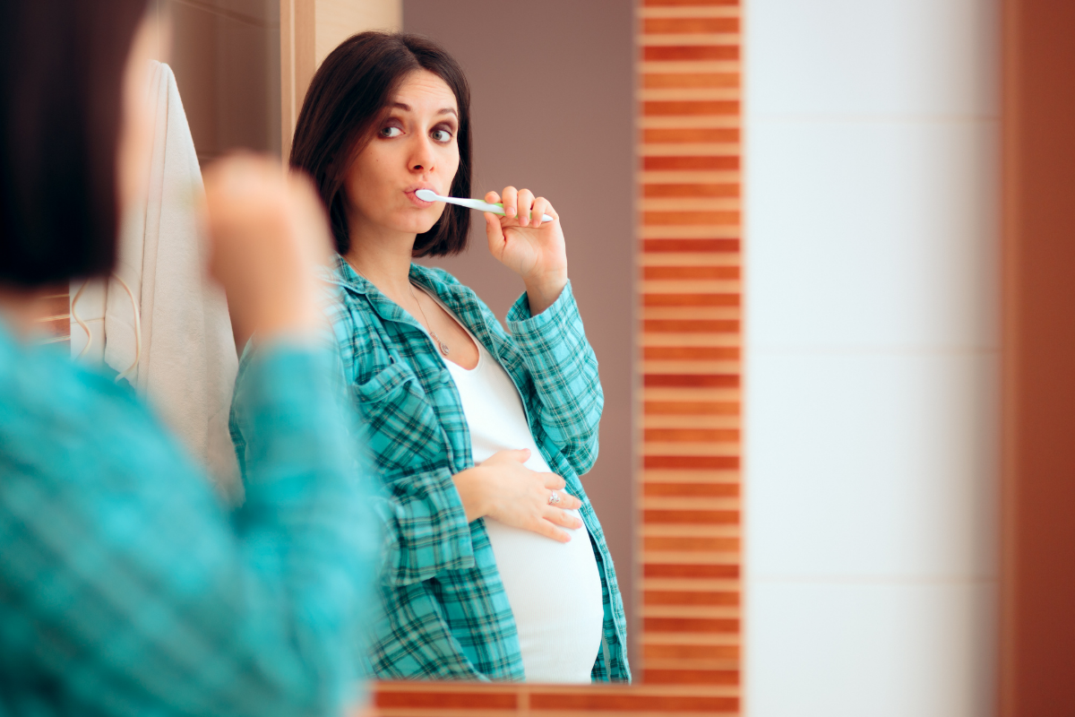 pregnant woman brushes her teeth in the mirror