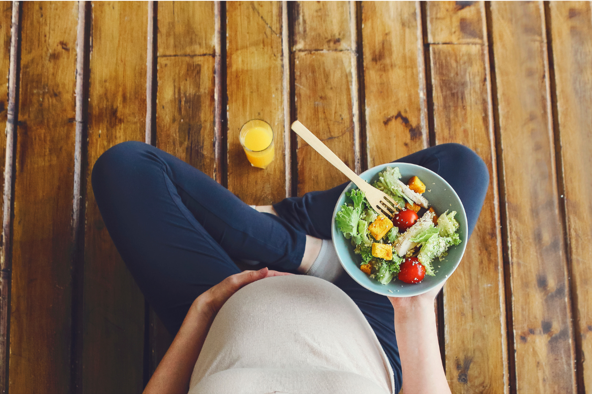 pregnany woman eats a salad sitting on the floor