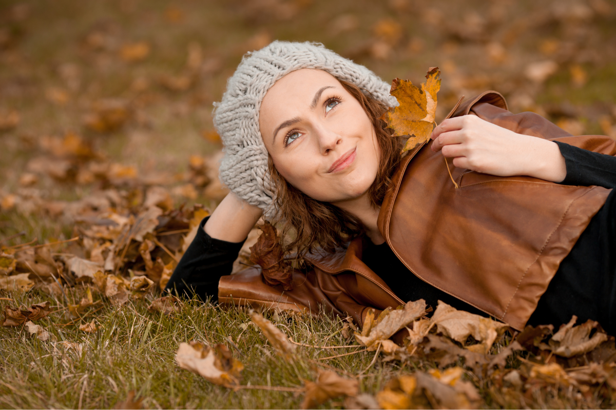 γυναίκα με εποχική τριχόπτωση ξαπλώνει σε φύλλα φθινοπώρου